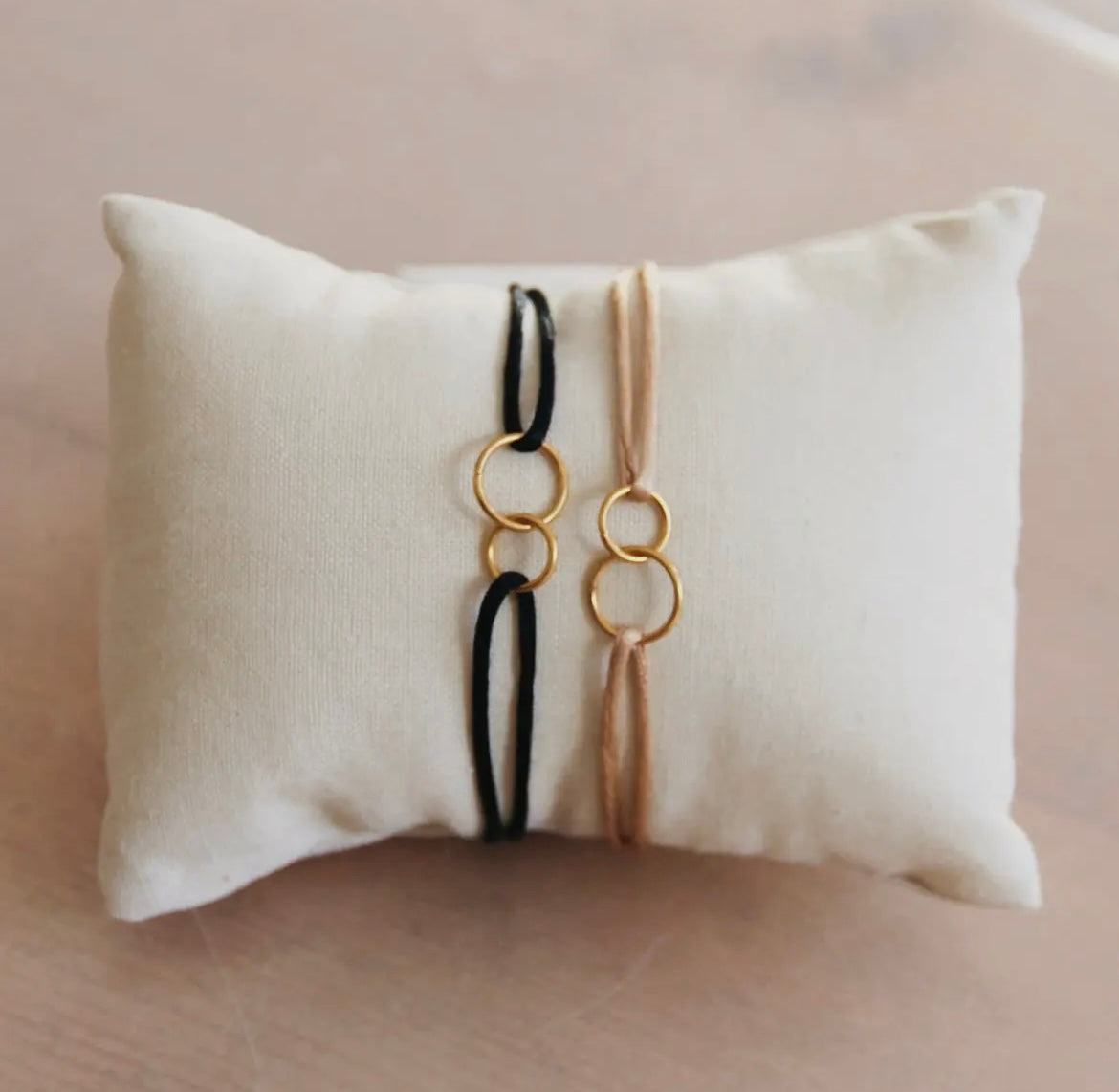 Nude farbenes Satinarmband mit zwei ineinander liegenden goldenen Ringen für die Unendlichkeit. Verstellbar über die Schiebeknoten.