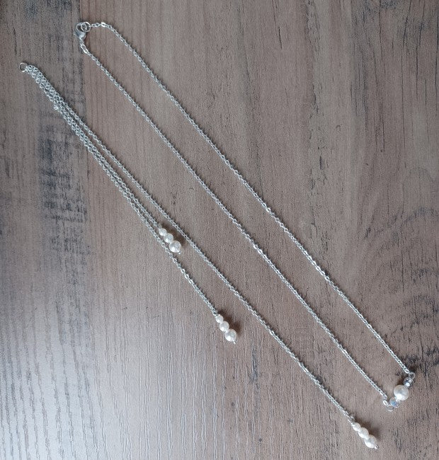 Silberne Rücken Halskette mit feiner Gliederkette mit einer Perle und zwei klaren Kristallperlen vorne. Im Rückenbereich mit drei unterschiedlich langen hängenden Gliederketten, am Ende mit je drei unterschiedlich großen Perlen! Rückenteil ist abnehmbar !