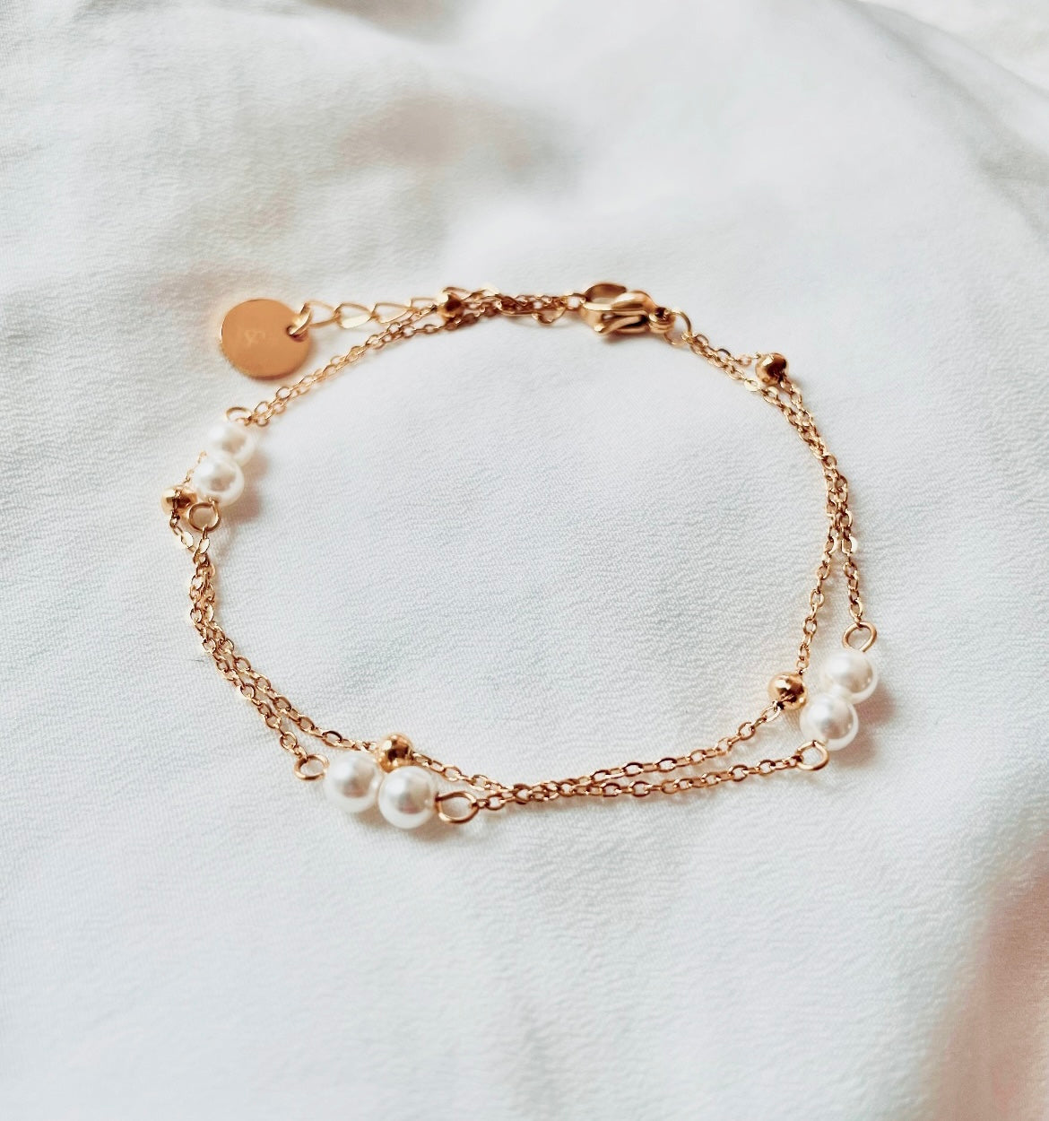 Filigranes Edelstahl Armband in Gold, aus zwei Reihen von Gliedeketten mit weißen Perlen und kleinen Edelstahlkügelchen.