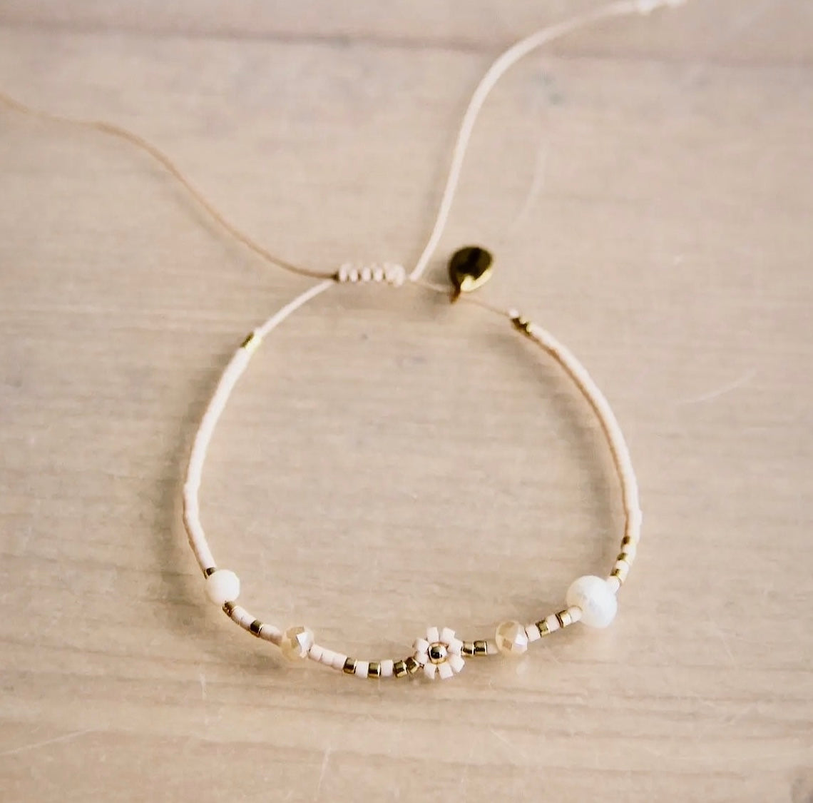 Miyuki-Armband in den Farben Nude und Gold mit facettierte Perlen und eine Gänseblümchenblume. Mit Schiebeknoten individuell verstellbar.