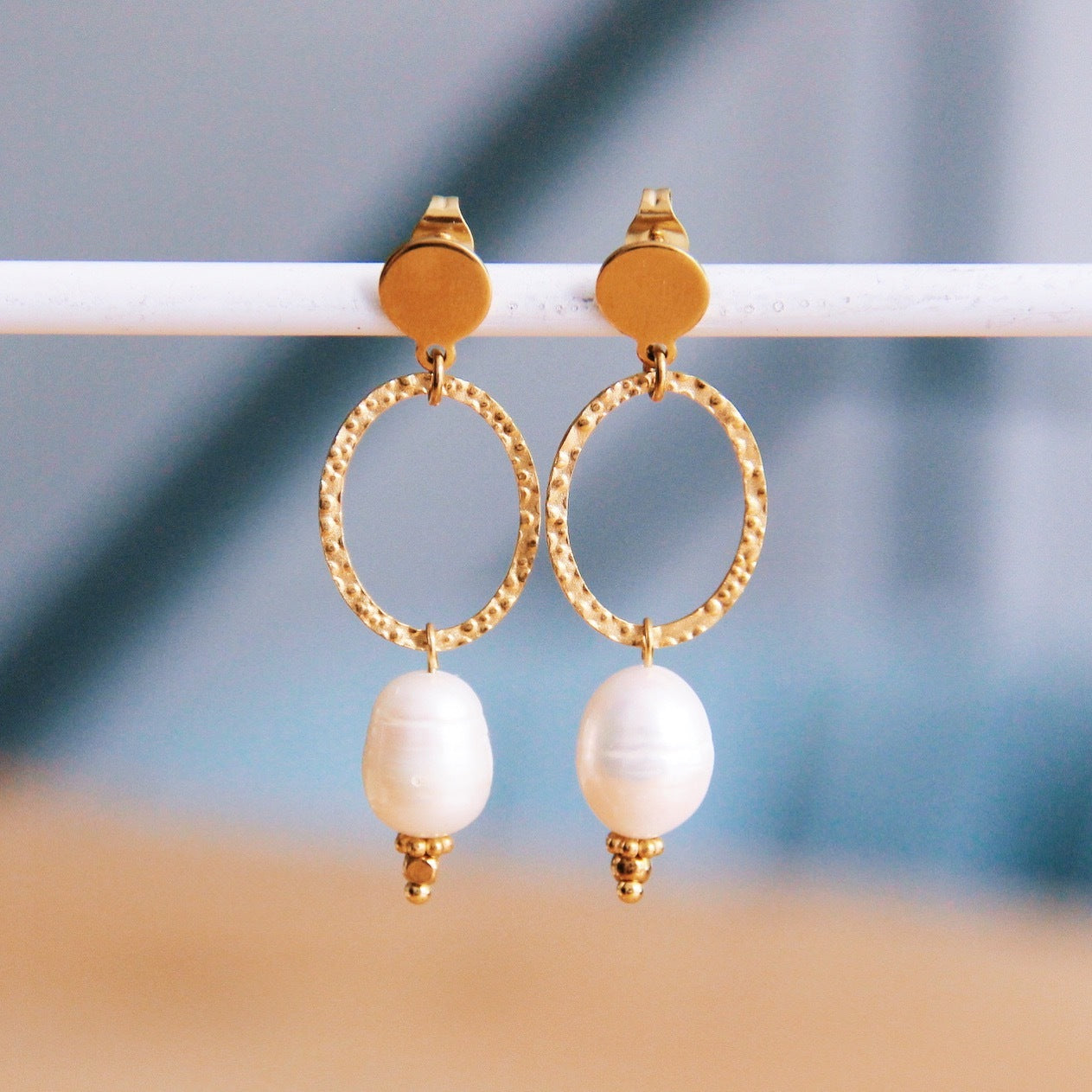 Edelstahl Ohrringe in Gold mit ovalem Anhänger mit gehämmerter Optik und ovaler weißer Perle hängend