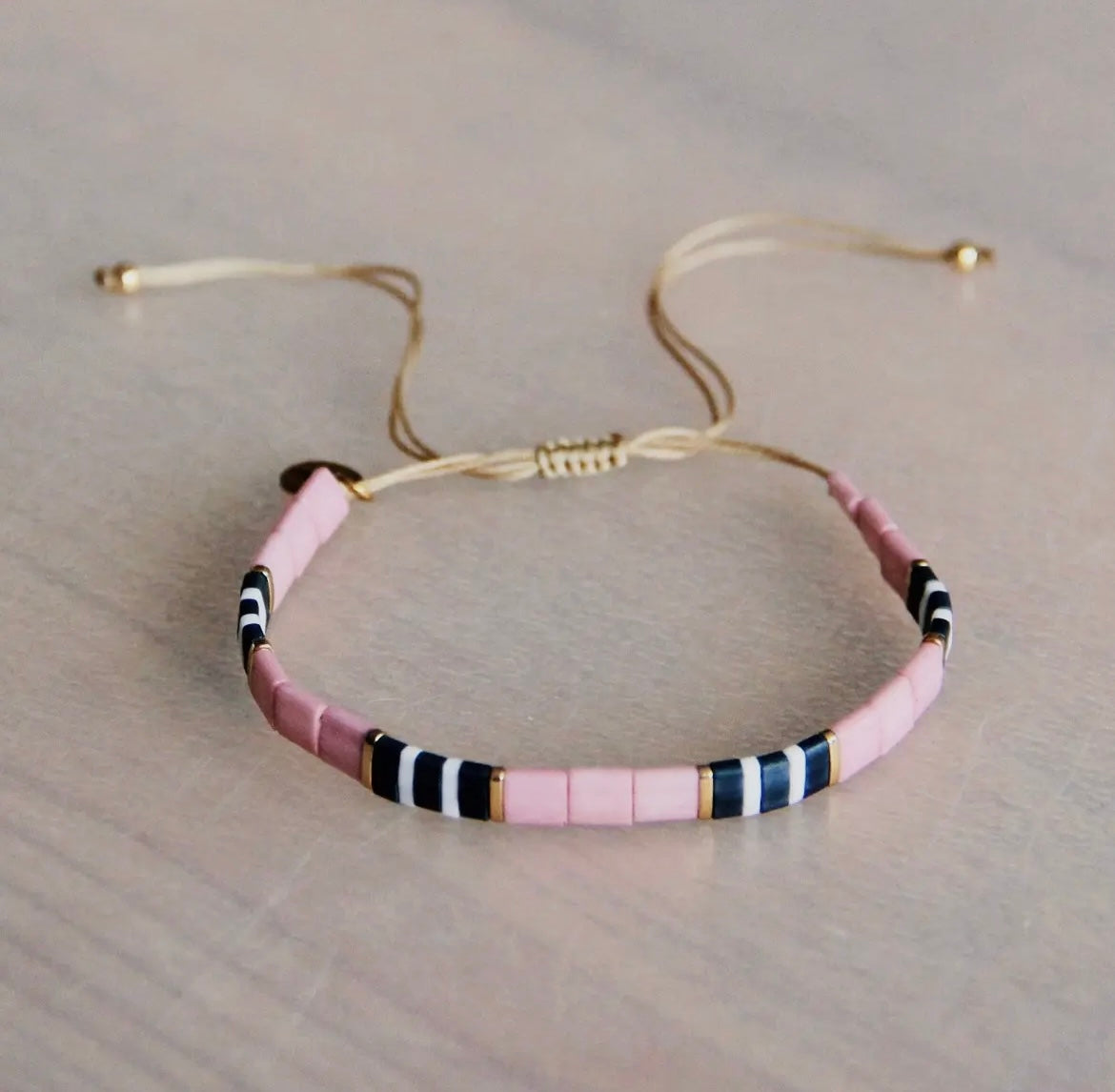Tilabead-Armband in den knalligen Farben lila, grau und weiß mit vergoldeten Perlen. Mit Schiebeknöpfe individuell in der Größe verstellbar.