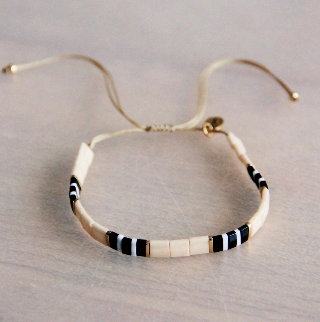 Hübsches gewebtes Armband in der Farbe nude, schwarz weiß und vergoldeten Perlen. Durch den Schiebeknoten ist es variabel verstellbar. Mit Tilabead Miyuki Perlen handgearbeitet.