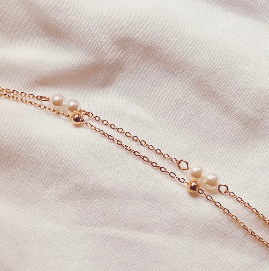 Filigranes Edelstahl Armband in Gold, aus zwei Reihen von Gliedeketten mit weißen Perlen und kleinen Edelstahlkügelchen.