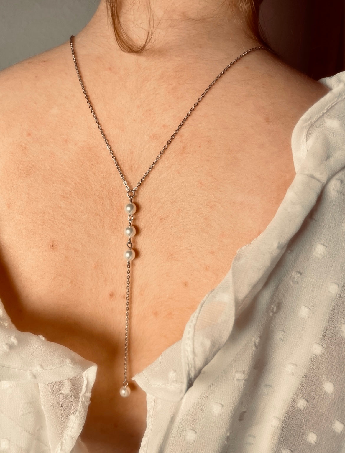 Silberne Rücken Halskette aus einer feinen Gliederkette mit einer Perle vorne. Im Rückenbereich ist sie hängend mit drei untereinander gereihten Perlen und einer Perle am Ende versehen.