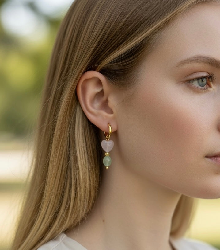 Feine Edelstahl Creolen in sanften Farben. An jeder Creole hängt ein Anhänger mit einem facettierten Rosenquarz-Herz von 8 mm, gefolgt von einer kleinen Perle und einem ovalen Peridot-Stein von 5 x 6 mm. Eine Kombination aus zarten Rosa- und frischen Grüntönen.
