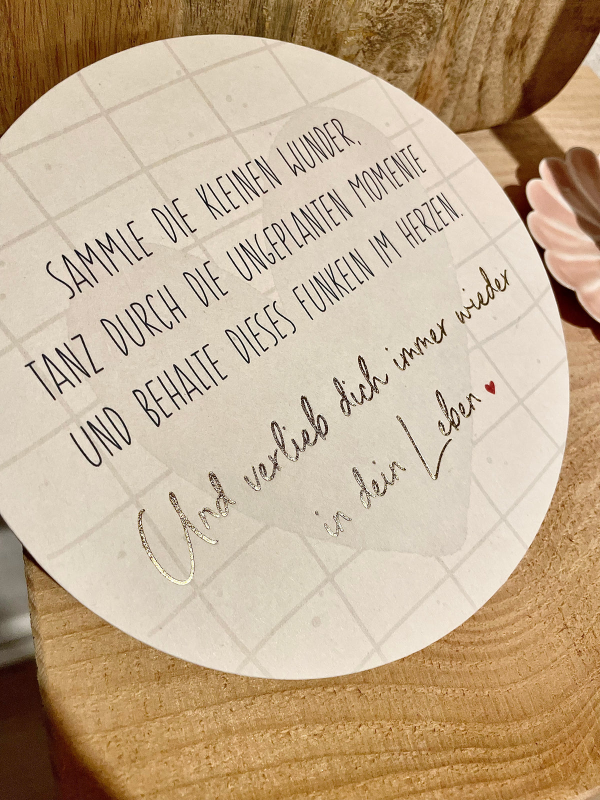 Rund Papier Karte mit 15cm Durchmesser. Stehend auf Holzaufsteller mit der Aufschrift:
„Sammle die kleinen Wunder. Tanz durch die ungeplanten Momente und behalte dieses Funkeln im Herzen. Und verlieb dich immer wieder in dein Leben.“
