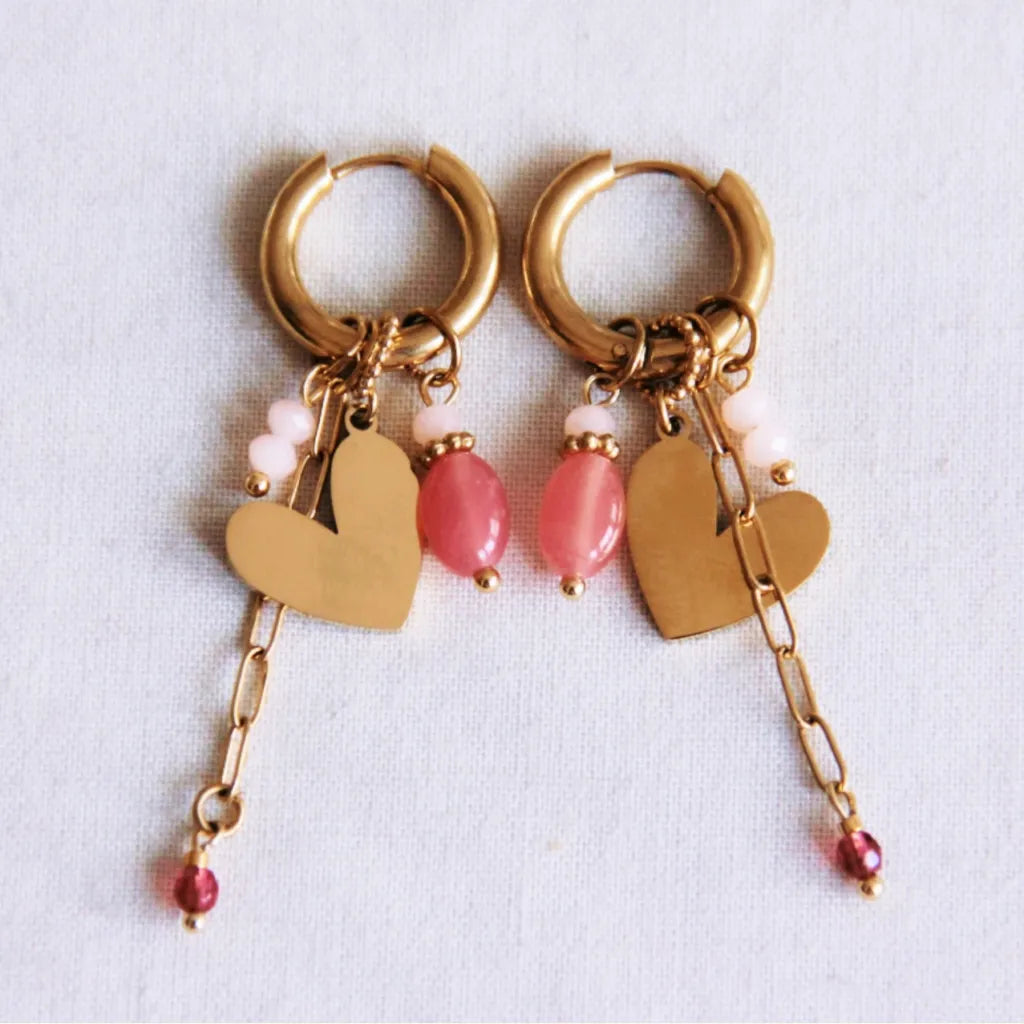 In goldene Click Creole ist ein gedrehter Ring eingehangen mit poliertem Herzchen. Zudem sind weitere kleine rosa Steinchen eingehangen und ein kleines Edelstahlkettchen