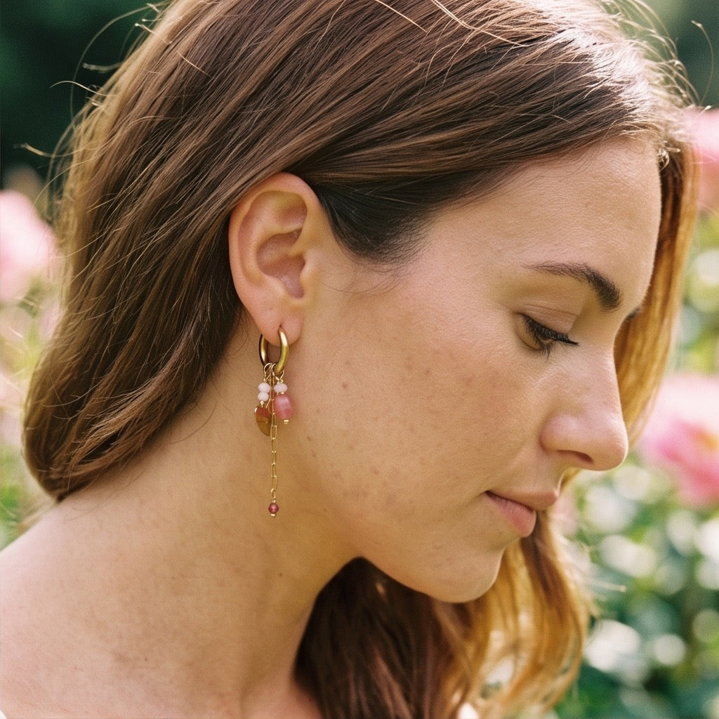 In goldene Click Creole ist ein gedrehter Ring eingehangen mit poliertem Herzchen. Zudem sind weitere kleine rosa Steinchen eingehangen und ein kleines Edelstahlkettchen