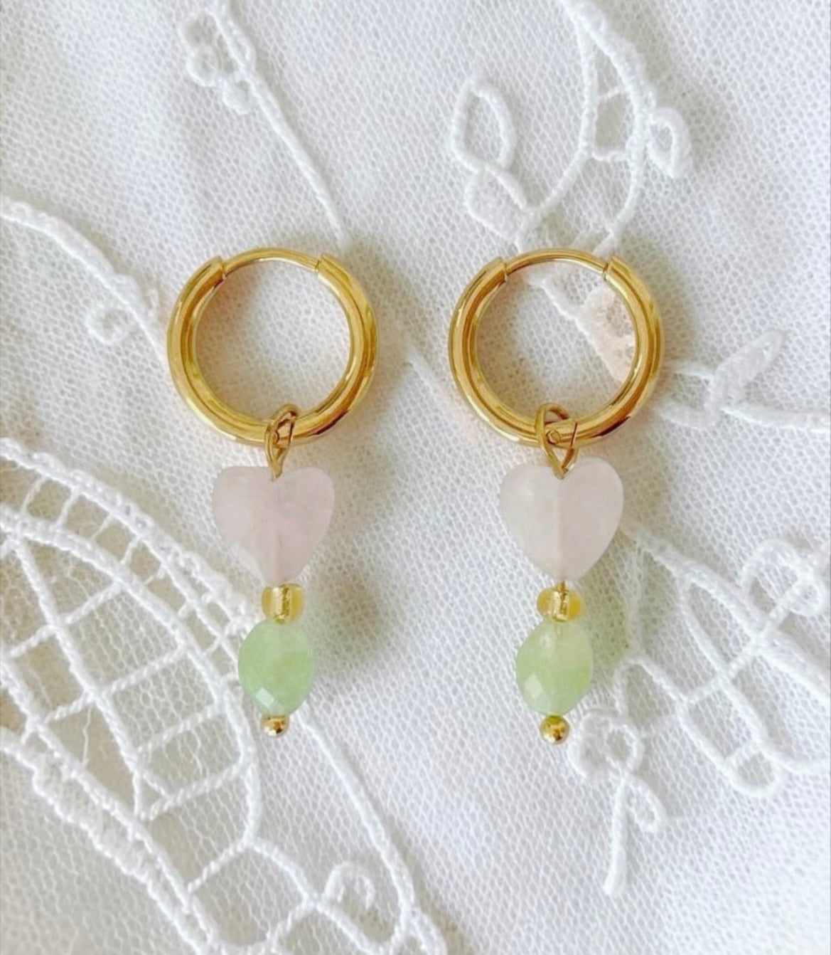 Feine Edelstahl Creolen in sanften Farben. An jeder Creole hängt ein Anhänger mit einem facettierten Rosenquarz-Herz von 8 mm, gefolgt von einer kleinen Perle und einem ovalen Peridot-Stein von 5 x 6 mm. Eine Kombination aus zarten Rosa- und frischen Grüntönen.