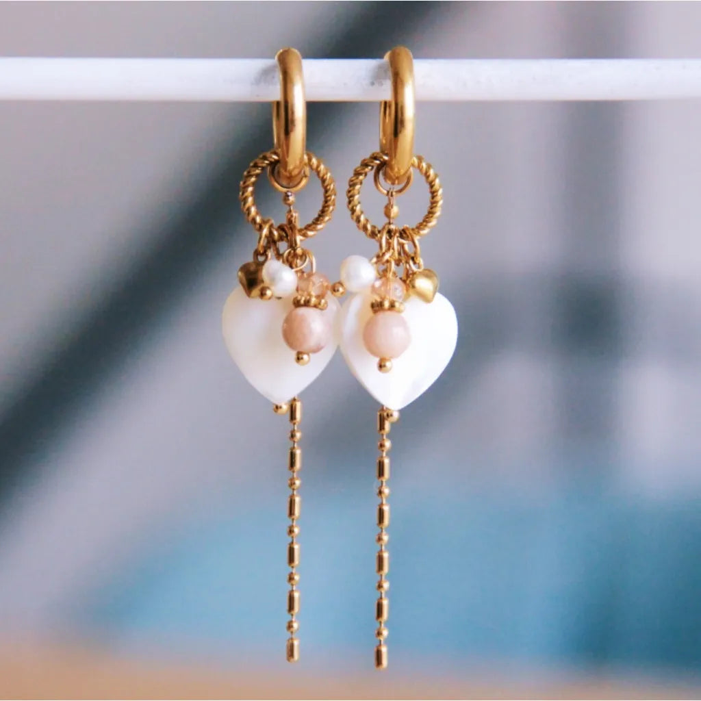 In die Goldene Click Creole ist ein gedrehter Ring eingehangen. An dem Ring hängt ein weißes Perlmutt Herz. Zudem sind weitere kleine Steinchen in nude und weiß
