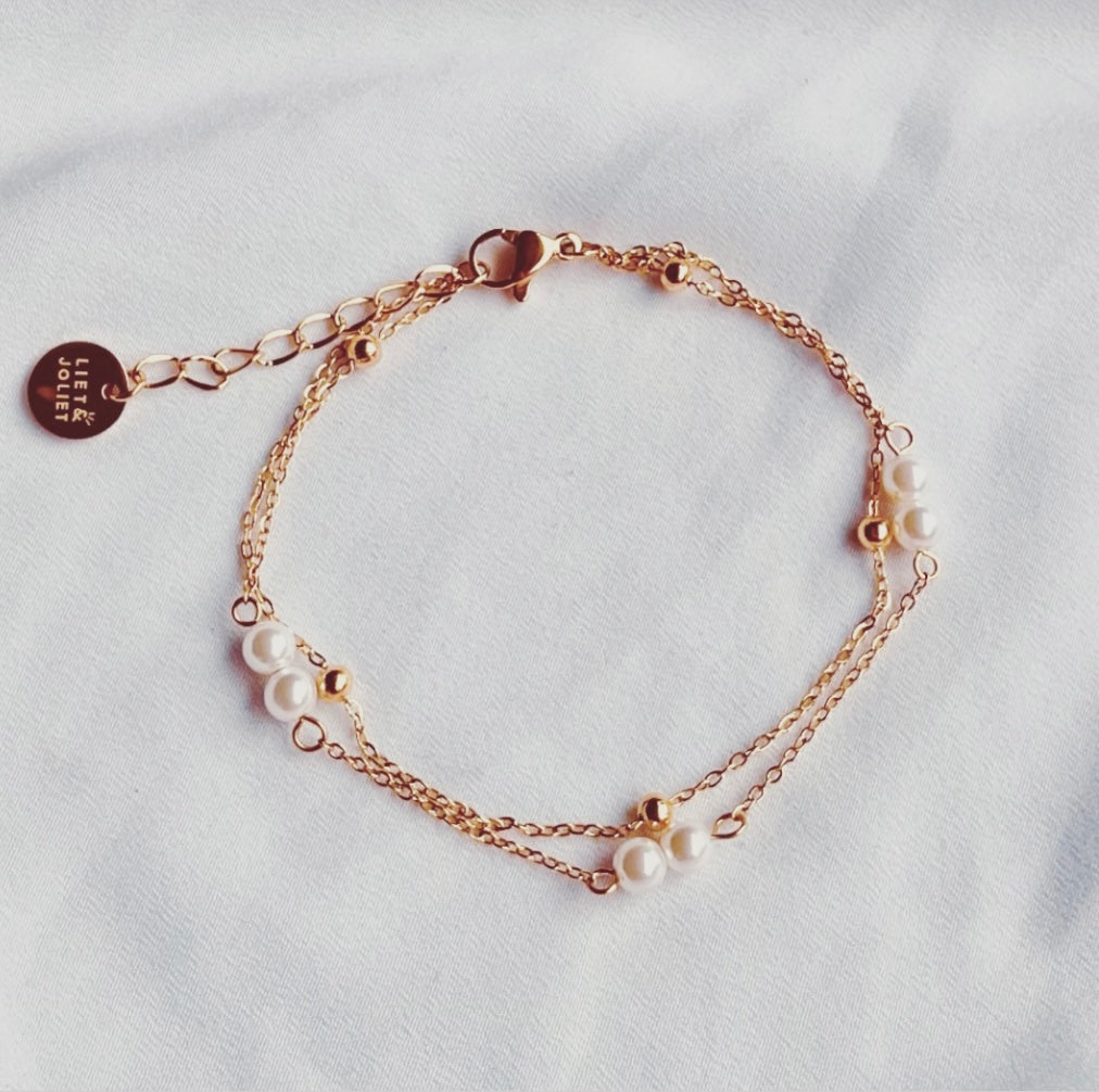 Filigranes Edelstahl Armband in Gold, aus zwei Reihen von Gliedeketten mit weißen Perlen und kleinen Edelstahlkügelchen.