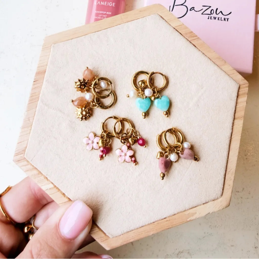 In die goldene Click Creole ist eine Rosa Perlmutt Blume, ein kleines Herzchen und rosa, pinke Steinchen eingehangen. Die Anhänger sind herausnehmbar.