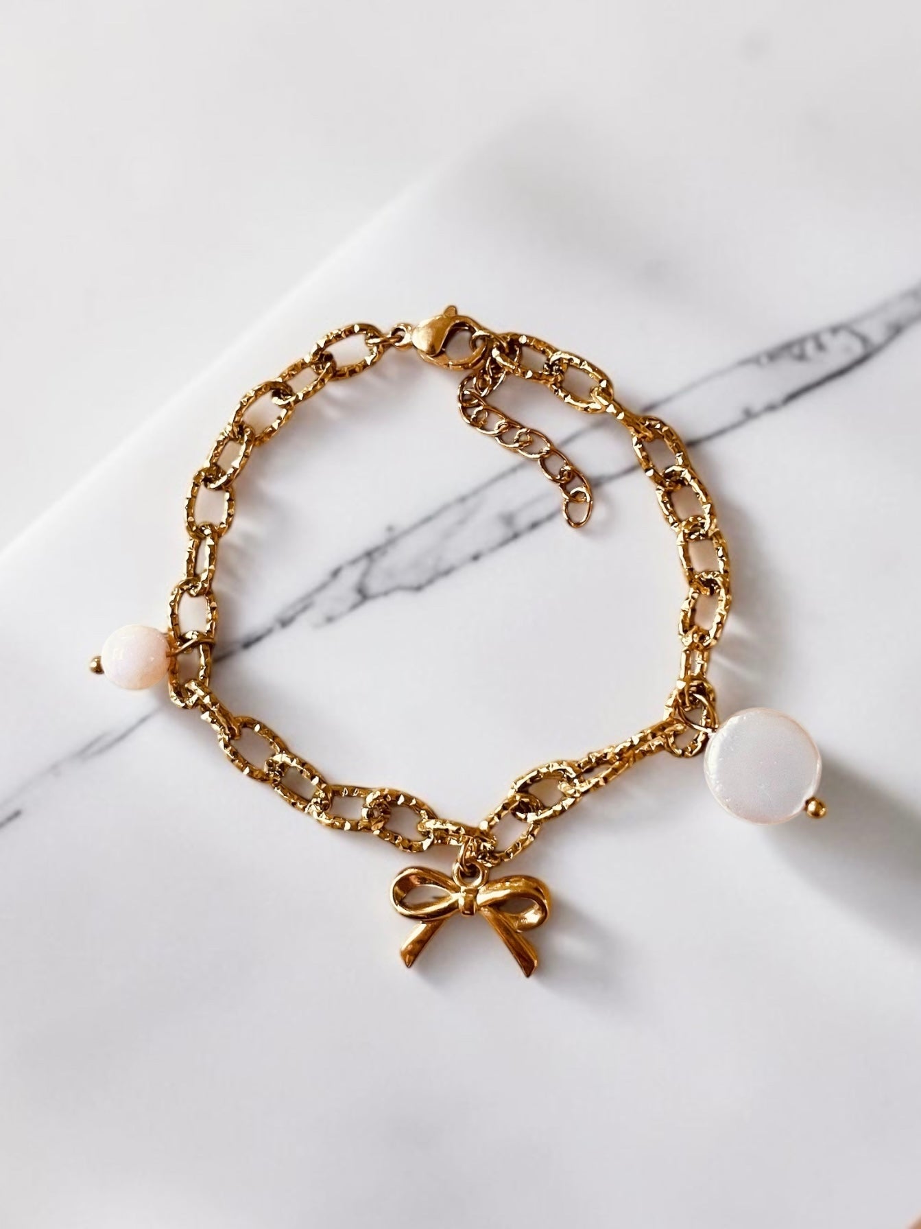 Edelstahl Armband mit länglichen groben Gliedern. Eingehängt sind drei verschiedene Anhänger.
Ein runder Muschel-Anhänger mit natürlichem, sommerlichem Look
Eine kleine Schleife für einen femininen, verspielten Touch und ein persischer Jaspis Stein.