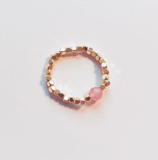Elastische Edelstahlring, rundherum mit kleinen Edelstahl Würfeln und in der Mitte ein rosa Naturstein. 