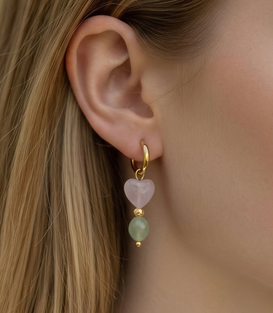 Feine Edelstahl Creolen in sanften Farben. An jeder Creole hängt ein Anhänger mit einem facettierten Rosenquarz-Herz von 8 mm, gefolgt von einer kleinen Perle und einem ovalen Peridot-Stein von 5 x 6 mm. Eine Kombination aus zarten Rosa- und frischen Grüntönen.