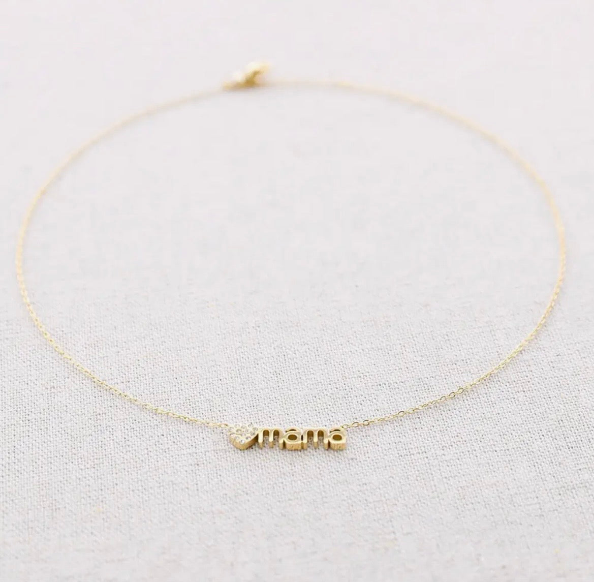 Feine goldene Edelstahl Kette  aus einer feinen Gliederkette mit einem Verlängerungskettchen. In der Mitte ist ein goldenes Herzchen mit kleinen Zirkoniasteinchen und dem Schruftzug „MAMA“ eingearbeitet.