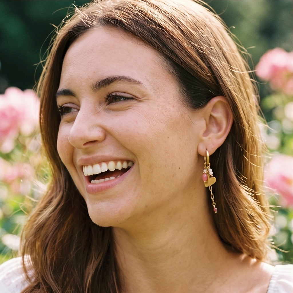 In goldene Click Creole ist ein gedrehter Ring eingehangen mit poliertem Herzchen. Zudem sind weitere kleine rosa Steinchen eingehangen und ein kleines Edelstahlkettchen