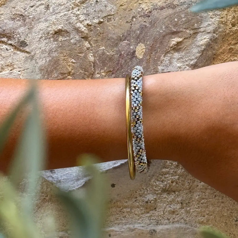 Graublau-goldenes Glasperlenarmband am Handgelenk kombiniert mit weiterem Gold-Schmuck, fair produziert in Nepal
