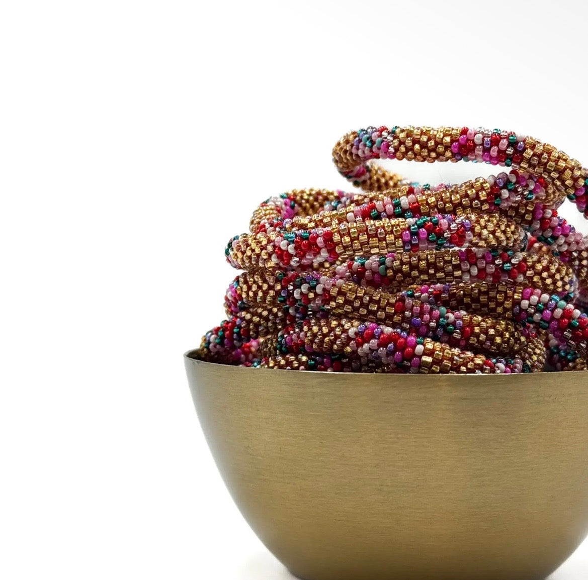 Glasperlen Armband liegend in goldener Schale in der Farbe Gold,  kräftiges Rot, Türkis, Weiß und zartes Flieder.