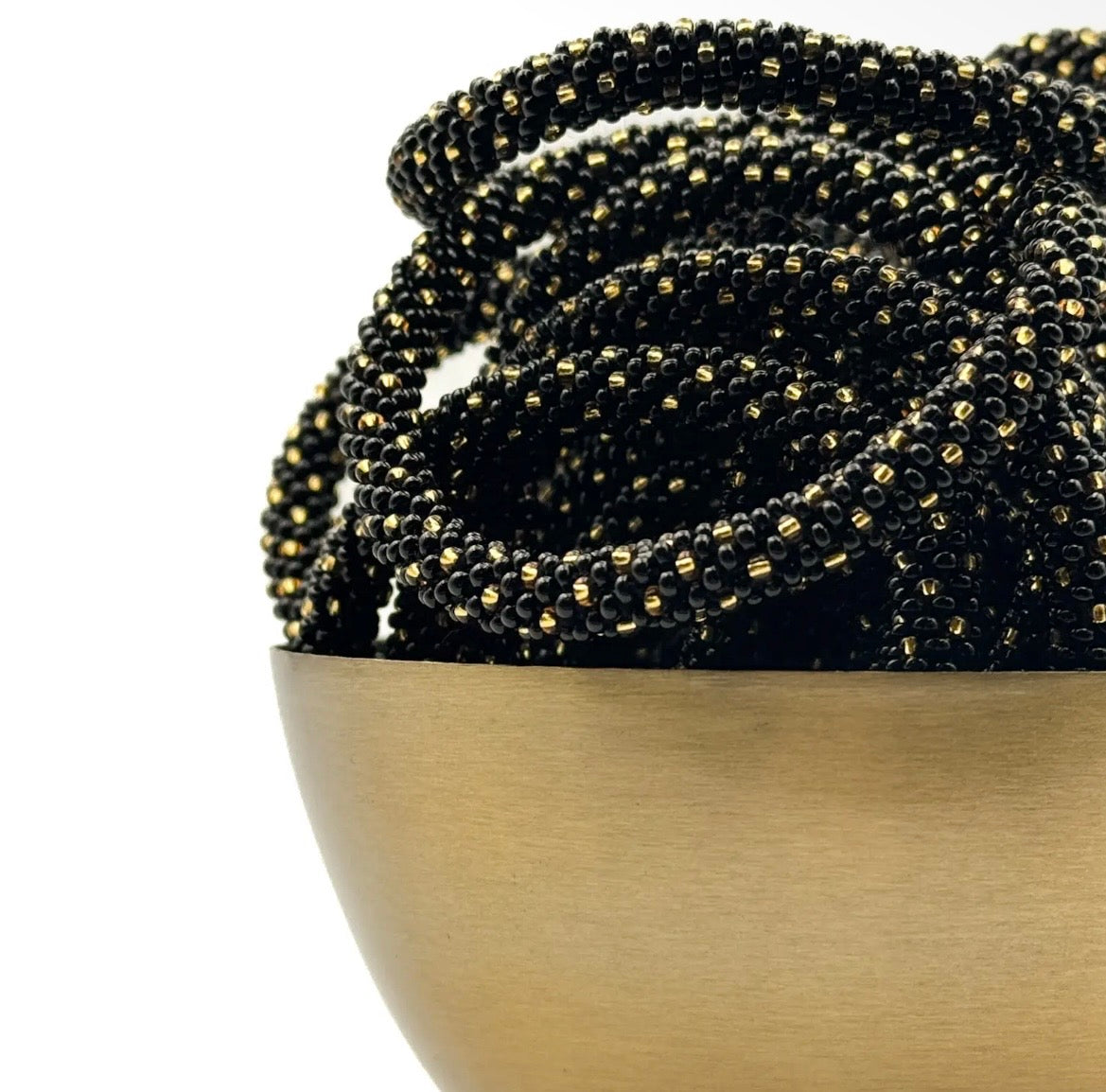 Handgefertigtes Glasperlen Armband in schwarz mit goldenen Tupfen in goldener Schale liegend.