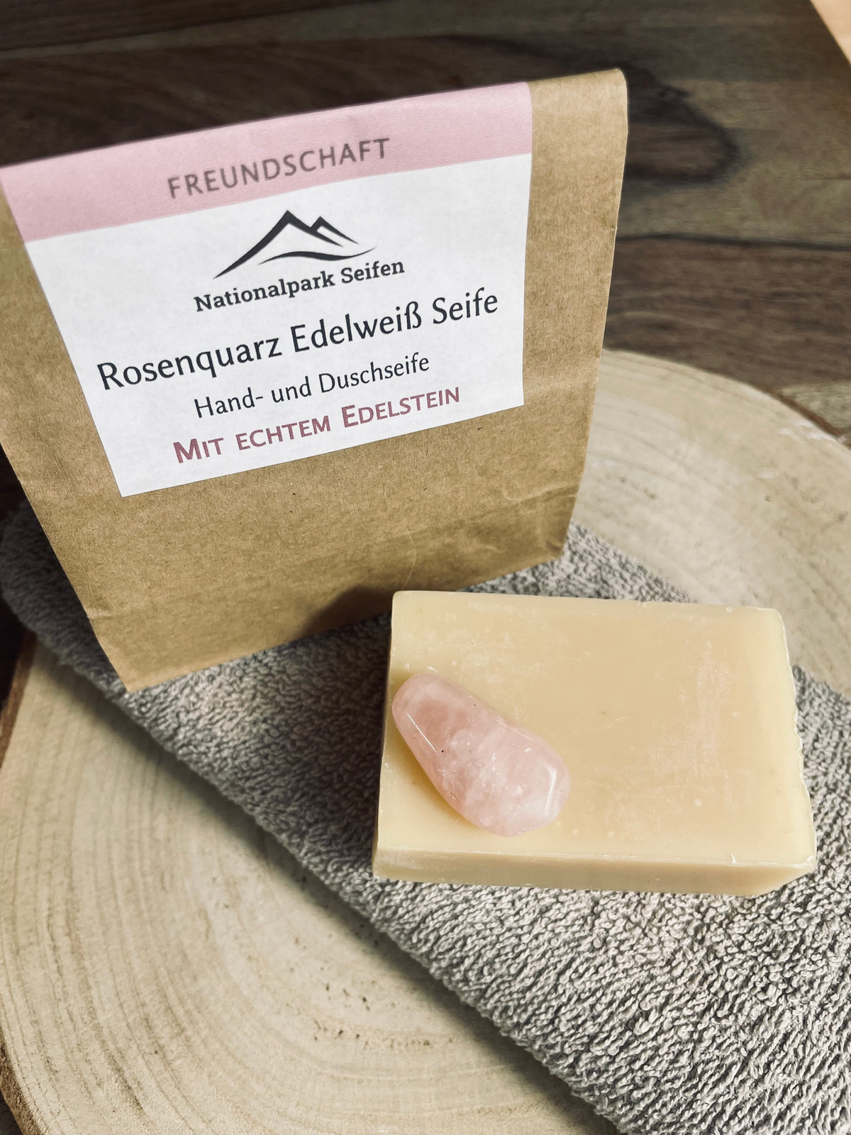 Rosenquarz Stein als stein der liebe liegend auf Naturseife mit Papiertütchen im Hintergrund und blumigen Duft der Seife.
